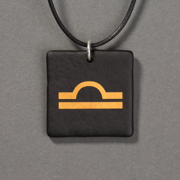 Sandcarved gold and black glass libra pendant.